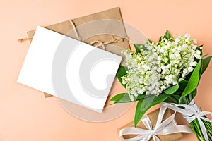 Blank greeting card with Lily of the valley flowers bouquet and gift box on peach color background. Wedding invitation