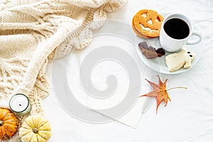 Blank greeting card mockup whit cup of coffee and cookies. Autumn, fall, halloween concept. Pumpkins and candle on white woolen