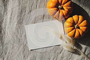 Blank greeting card, orange pumpkins, dry grass on textile background, top view. Thanksgiving day greeting card design. Autumn,