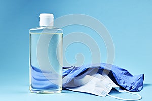 blank hand sanitizer with face mask and latex gloves over blue background. copy space. covid-19 symbol concept