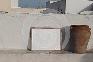 Blank horizontal wooden frame picture mock up. Vintage olive clay storage pot, vase. White old textured white wall in