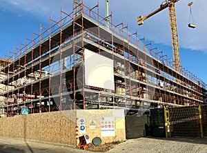 Blank information board hanging on the scaffoldings around the new building under construction. Warning signs at the bottom.