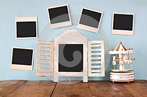 Blank instant photos hang over wooden textured background next to blank blackboard and vintage white carousel horses