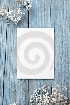 Blank invitation card mockup, white greeting card with floral decor on blue wooden background. Greeting card mock up with elegant