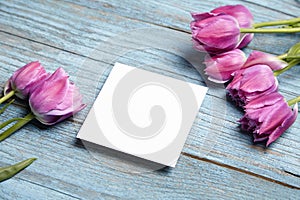 Blank invitation card mockup, white square greeting card with purple flower on blue wooden background. blank flyer on rustic blue