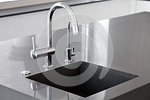 Blank kitchen sink of dark gray marble with chrome tap in a clean kitchen.