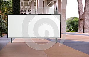 Blank large billboard advertising banner mockup in a large open space with plants under a modern bridge. Large horizontal digital