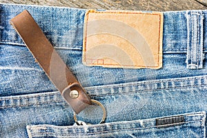 Blank leather jeans label on a blue jeans, wooden background.