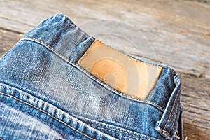 Blank leather jeans label on a blue jeans, wooden background.