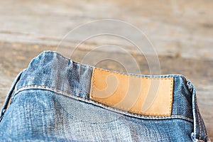 Blank leather label blue jeans on wooden background.