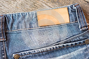 Blank leather label blue jeans on wooden background.