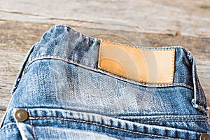 Blank leather label blue jeans on wooden background.