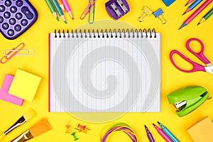 Blank, lined, notebook with school supplies frame against a yellow background. Back to school. Copy space.