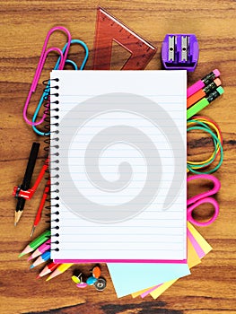 Blank lined notebook with underlying school supply frame on wood