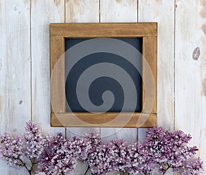 A blank mock-up with a warm-coloured wooden blackboard frame and purple lilac flowers