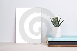 Blank mockup paper sheet copy space and plants in potted on book on wooden table, poster and invitation with empty on desk.