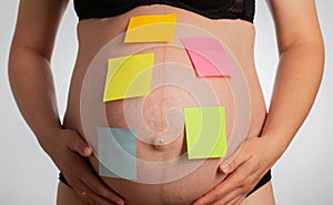 Blank multi-colored stickers are glued on the belly of a pregnant girl. In anticipation of the birth of a child