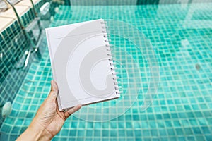 Blank note book in girl hand over blurred swimming pool background, outdoor day light