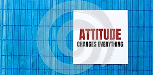 Blank note pad with ATTITUDE CHANGES EVERYTHING text on blue wooden background