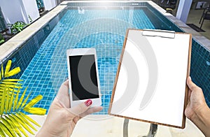 Blank note paper on wooden clipboard and smartphone in girl hand over clear swimming pool water background