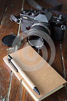 blank notebook with a ballpoint and old vintage photo camera on wooden background