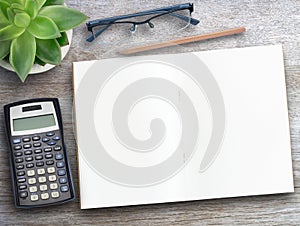 Blank notebook,calculator,earphone and cup of coffee with flower on wood table background