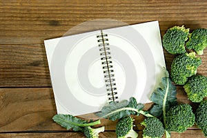 Blank notebook with fresh broccoli on wooden table