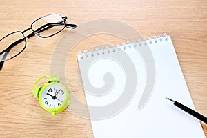 Blank notebook and pen with clock on a desk