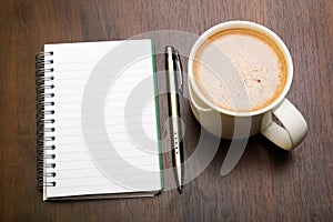 Blank notebook, pen and cup of coffee on wooden brown background,