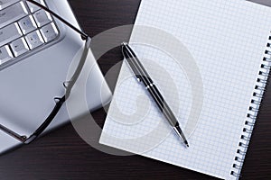 Blank notebook, pen, glasses and laptop