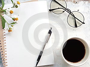 Blank notebook with pen and glasses next to a cup of coffee.