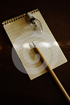 Blank notebook with pen and light bulb on a dark wooden table