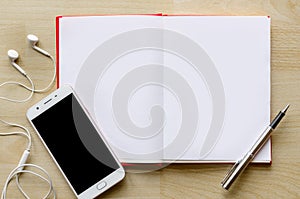 Blank notebook with pen on wood table And a wrist watch headset Modern phone Text input area