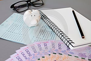 Blank notebook, pencil, savings account passbook, eye glasses, Thai money and piggy bank on gray background