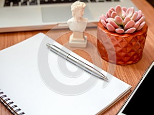 Blank notebook with smartphone, laptop computer and succulent plant in copper pot on wooden table background