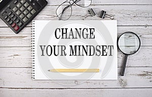 Blank notebook with text CHANGE YOUR MINDSET on white background with calculator and office tools