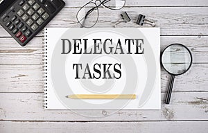 Blank notebook with text DELEGATE TASKS on the white background with calculator and office tools
