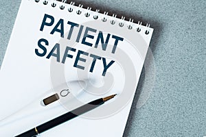 Blank notebook with thermometre and pen.on table. PATIENT SAFETY text
