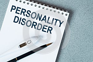 Blank notebook with thermometre and pen on table. Personality disorder text