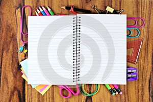 Blank notebook with underlying frame of school supplies over wood