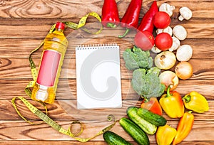 Blank notepad with bottle of cooking oil, different vegetables and measure tape on wooden background. Top view. Healthy food