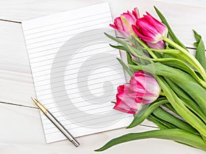 Blank notepad and bouquet with tulips on the wooden table. Top view