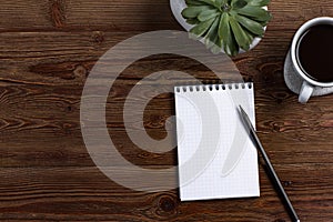 A blank Notepad with pencil, with coffee and plant on a wooden background