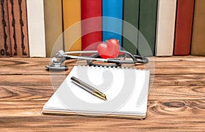 Blank notepad with stethoscope,red heart and books on wooden table