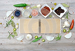 Blank open notebook for notes and pepper, bay leaf, rosemary, onions, salt, olive oil, soy sauce on a wooden table