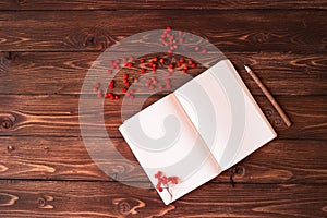 Blank open white notebook, wooden pencil and red ashberry on wooden background