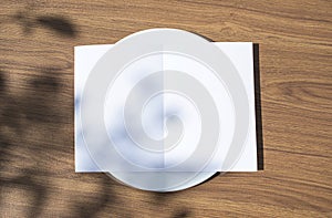 Blank opened bifold card on a classic empty white plate on the outdoor wooden table top view background as template for you design