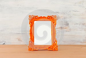 Blank orange photo frame over wooden table and white background. Ready for photography montage