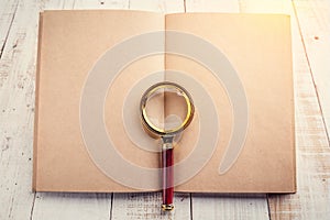 blank page notebook with a magnifying glass on a wooden background