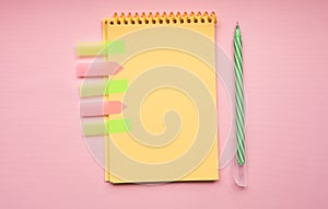 Blank page of vertical spiral note pad with pen on pink background